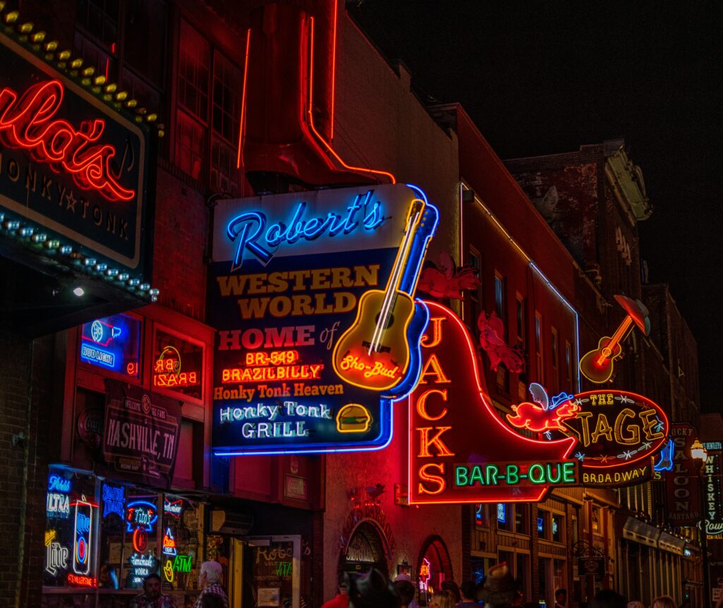 Close up shot of a street in downtown nashville at night. Signs shown are Jacks Bar-B-Que, The State Broadway, and Robert's Western World